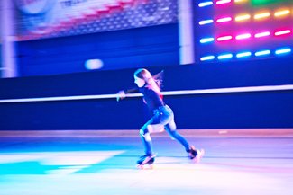 Girl skating fast on roller rink with lights